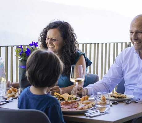 Familie sitzt am gedeckten Tisch auf der Restaurant-Terrasse des Familienhotels Familiamus