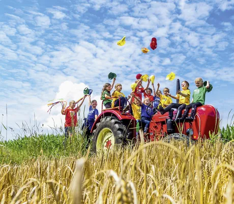 Kinder sitzen auf einem roten Traktor des Ulrichshof umgeben von Feldern