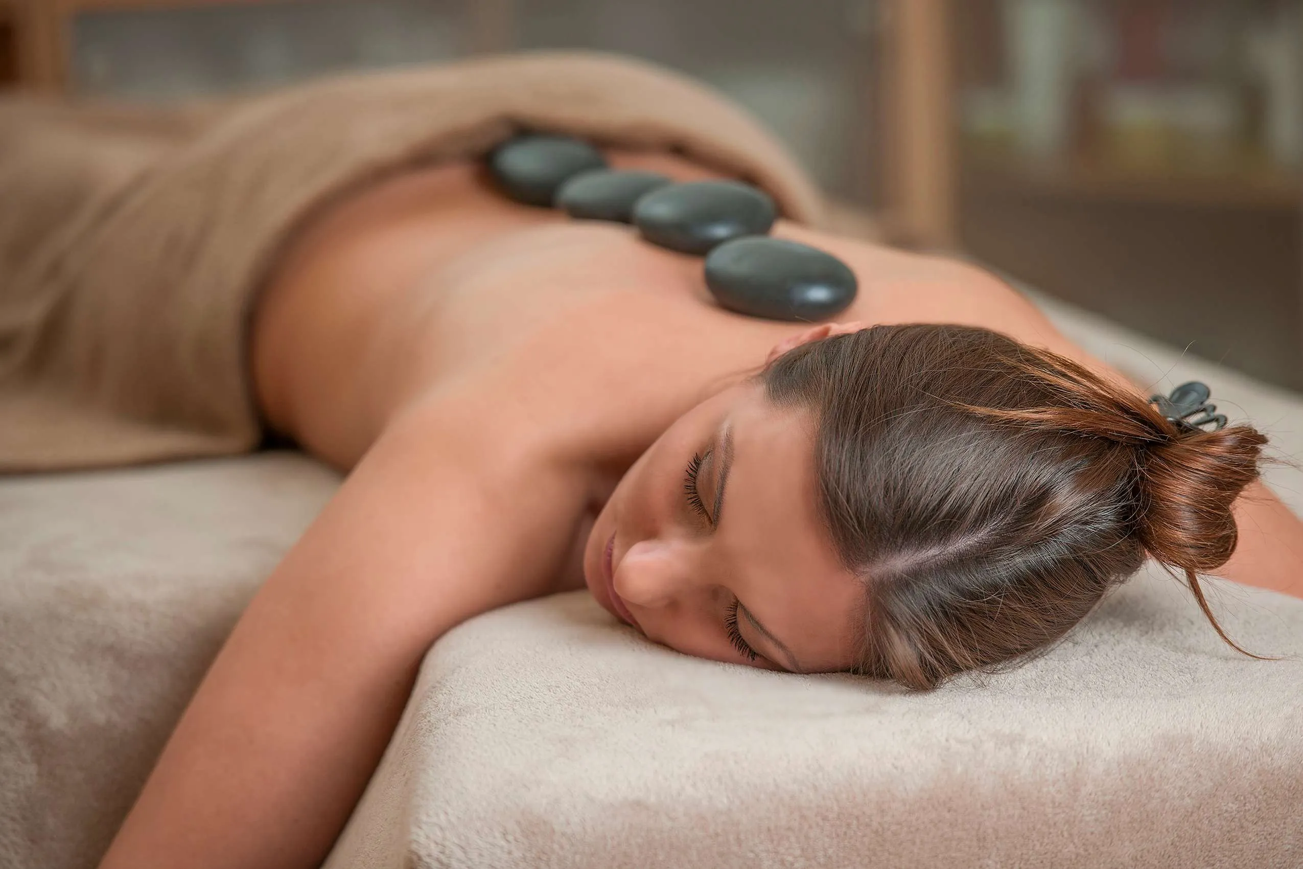 Auf dem Bauch liegende Frau mit vier Steinen auf dem R&uuml;cken bei HotStone-Anwendung im Bad Clevers Gesundheitsresort