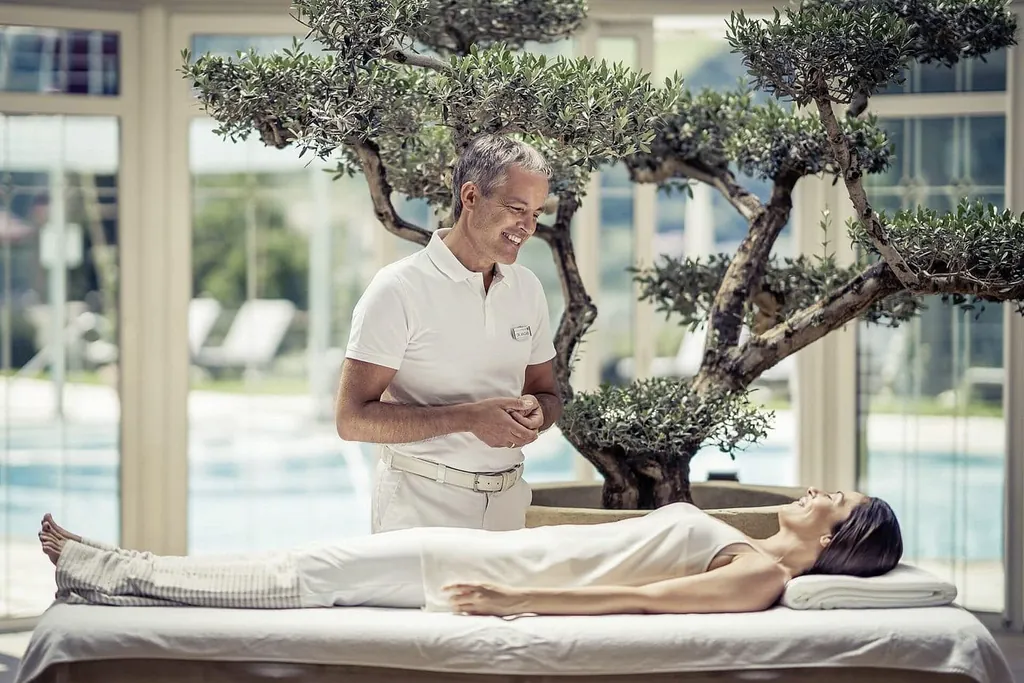 Arzt unterhält sich lächelnd mit weiblichem Preidl Medical Spa-Gast, der auf Behandlungsliege liegt, im Preidlhof Luxury DolceVita Resort