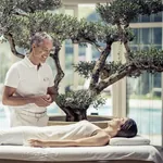 Arzt unterhält sich lächelnd mit weiblichem Preidl Medical Spa-Gast, der auf Behandlungsliege liegt, im Preidlhof Luxury DolceVita Resort