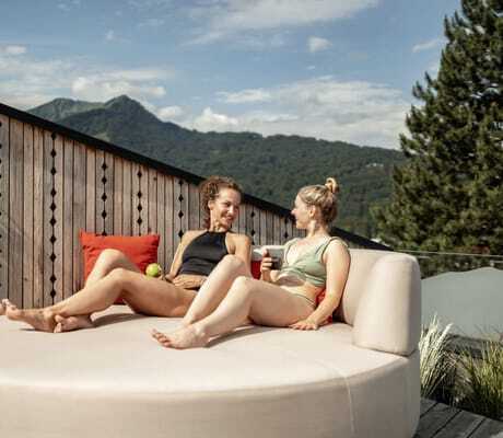Zwei Frauen sitzen auf einer Liege in der Rooftop-Area des Hotel Franks und lächeln sich an