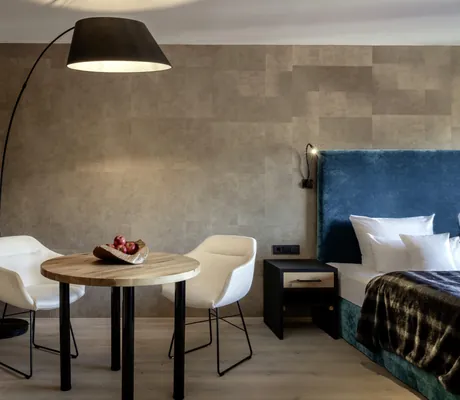 Wohnbereich eines Zimmers im Hotel Frank mit rundem Esstisch, zwei weißen Stühlen und großer Stehlampe