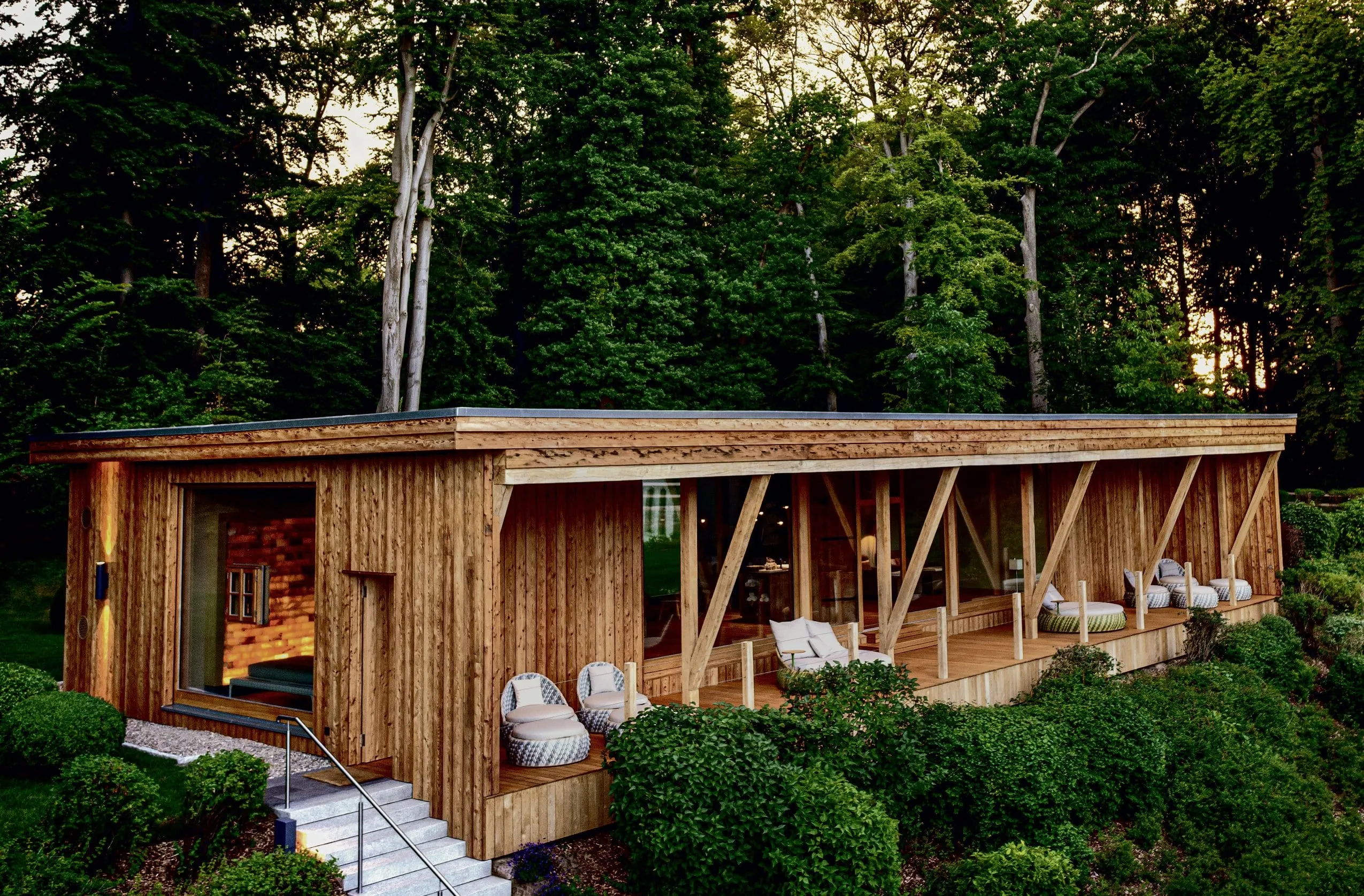 Holzbau des Solewaldraums im WEISSENHAUS Private Nature Luxury Resort mit Korbmöbeln auf der überdachten Terrasse