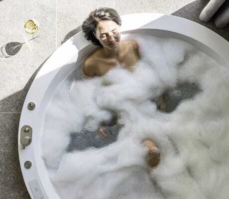 Frau liegt in runder Badewanne im Schaumbad im Hotel Weisses Kreuz