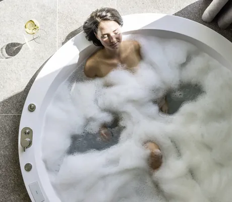 Frau liegt in runder Badewanne im Schaumbad im Hotel Weisses Kreuz