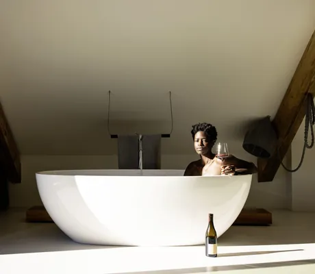 dunkelhäutige Frau liegt mit einem Glas Rotwein in der freistehenden Badewanne im Hotel Weisses Kreuz