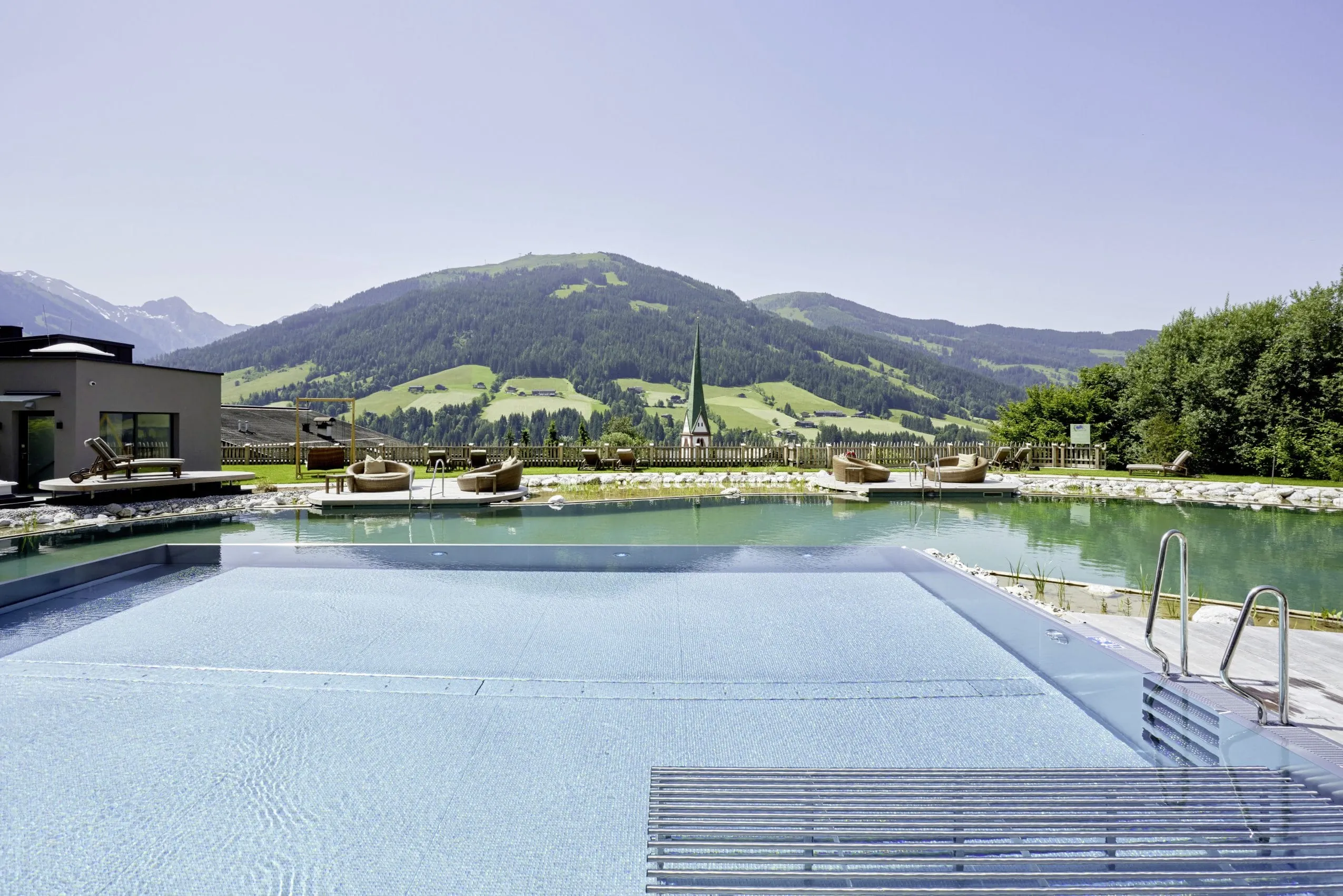 Outdoorpool und Naturbadteich im B&ouml;glerhof mit Blick auf die Kirche von Alpbach