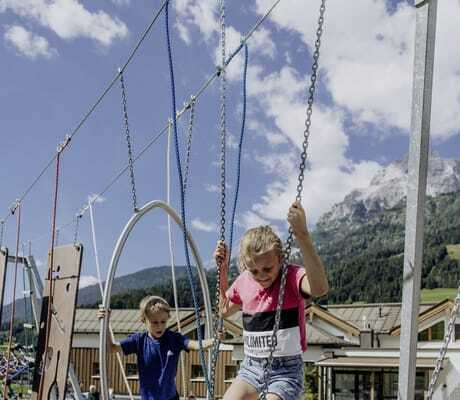 Mädchen in Shorts und Junge klettern über einen Parcours in der Riederalm