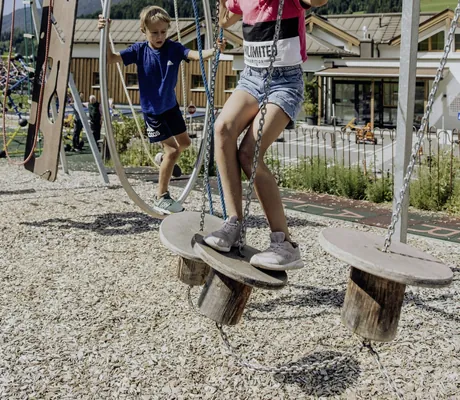 Mädchen in Shorts und Junge klettern über einen Parcours in der Riederalm