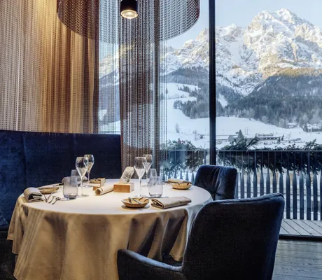 Restaurant mit blauen Samtsitzmöbeln in der Riederalm mit Blick auf die verschneiten Berge