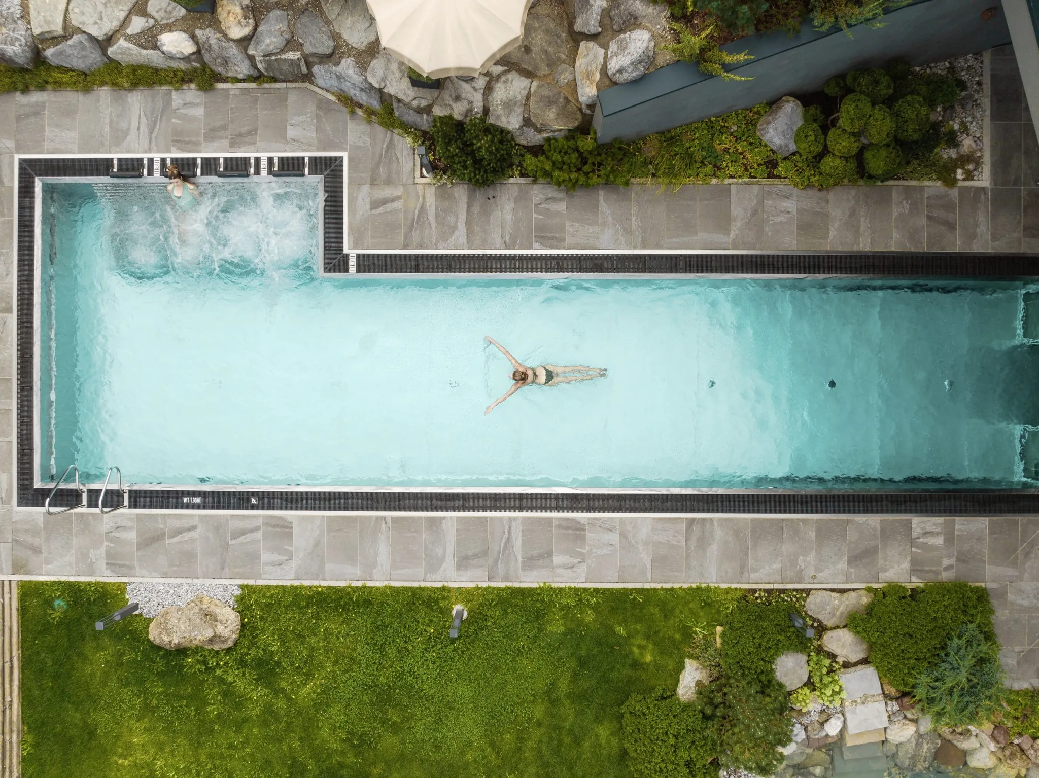 Blick von oben auf eine blonde Frau, die im Thermalwasserpool der Riederalm schwimmt