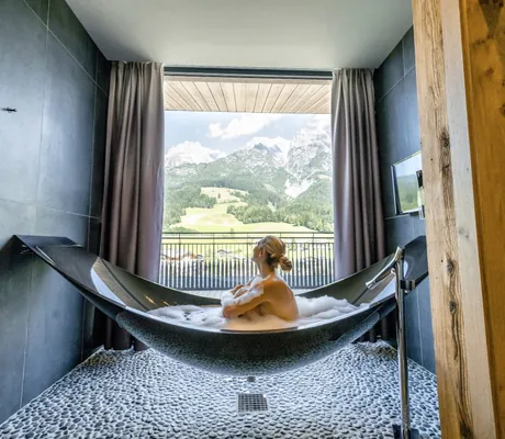 blonde Frau sitzt in frei schwebender schwarzer Badewanne in der Riederalm