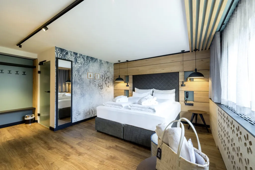 Blick in das Studio Alpin Deluxe des Hotel Schwarzbrunn im Holzdesign mit hohem Doppelbett, schwarzen Hängelampen, edler Tapete und Ganzkörperspiegel