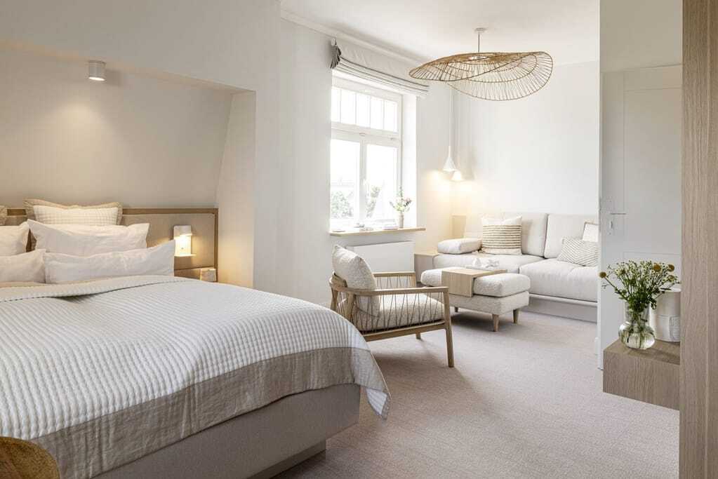 Doppelbett in der Villa Astoria mit beigefarbenem Sofa und Stuhl im Hintergrund