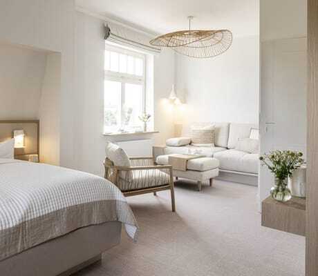 Doppelbett in der Villa Astoria mit beigefarbenem Sofa und Stuhl im Hintergrund