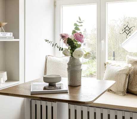 gemütliche helle Sitzbank mit drei beigefarbenen Kissen am Fenster der Villa Astoria mit kleinem Stehtisch