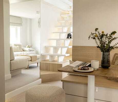 Blick in eine der hell eingerichteten Suiten der Villa Astoria mit Sitzbank, großem Spiegel und weißer Treppe im Hintergrund