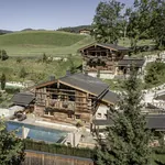 Außenansicht des urigen Bergdorfs Prechtlguts mit Blick auf die Pool Luxury Lodge mit großem Pool und Naturteich im Hintergrund