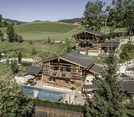 Außenansicht des urigen Bergdorfs Prechtlguts mit Blick auf die Pool Luxury Lodge mit großem Pool und Naturteich im Hintergrund