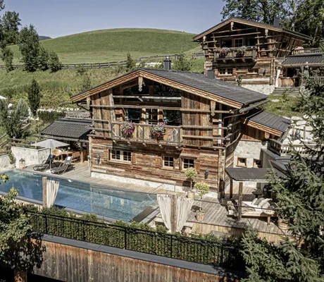 Blick auf die Pool Luxury Lodge des Bergdorf Prechtlgut mit großem Pool und Sonnenliegen im Vordergrund und weiterem Chalet im Hintergrund
