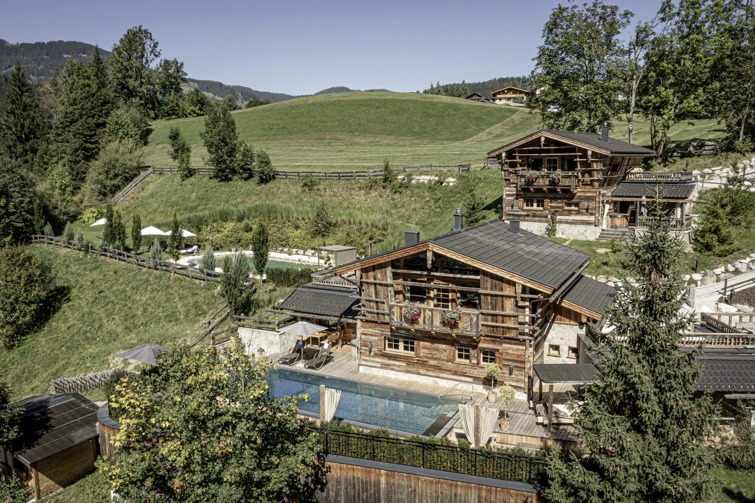 Außenansicht des urigen Bergdorfs Prechtlguts mit Blick auf die Pool Luxury Lodge mit großem Pool und Naturteich im Hintergrund