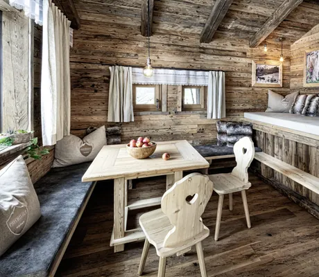 Essbereich eines der Chalets des Bergdorfs Prechtlgut mit Esstisch und Stühlen aus Holz und langer Sitzecke