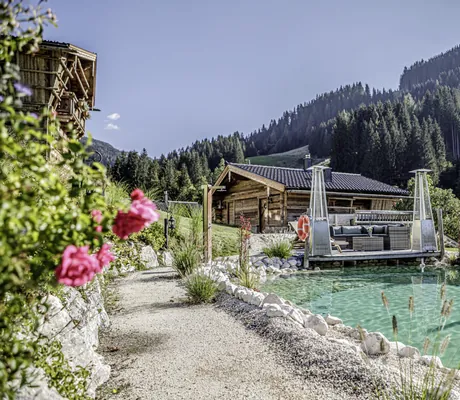 Naturteichanlage des Bergdorf Prechtlgut mit gemütlichem Loungebereich und Wäldern im Hintergrund