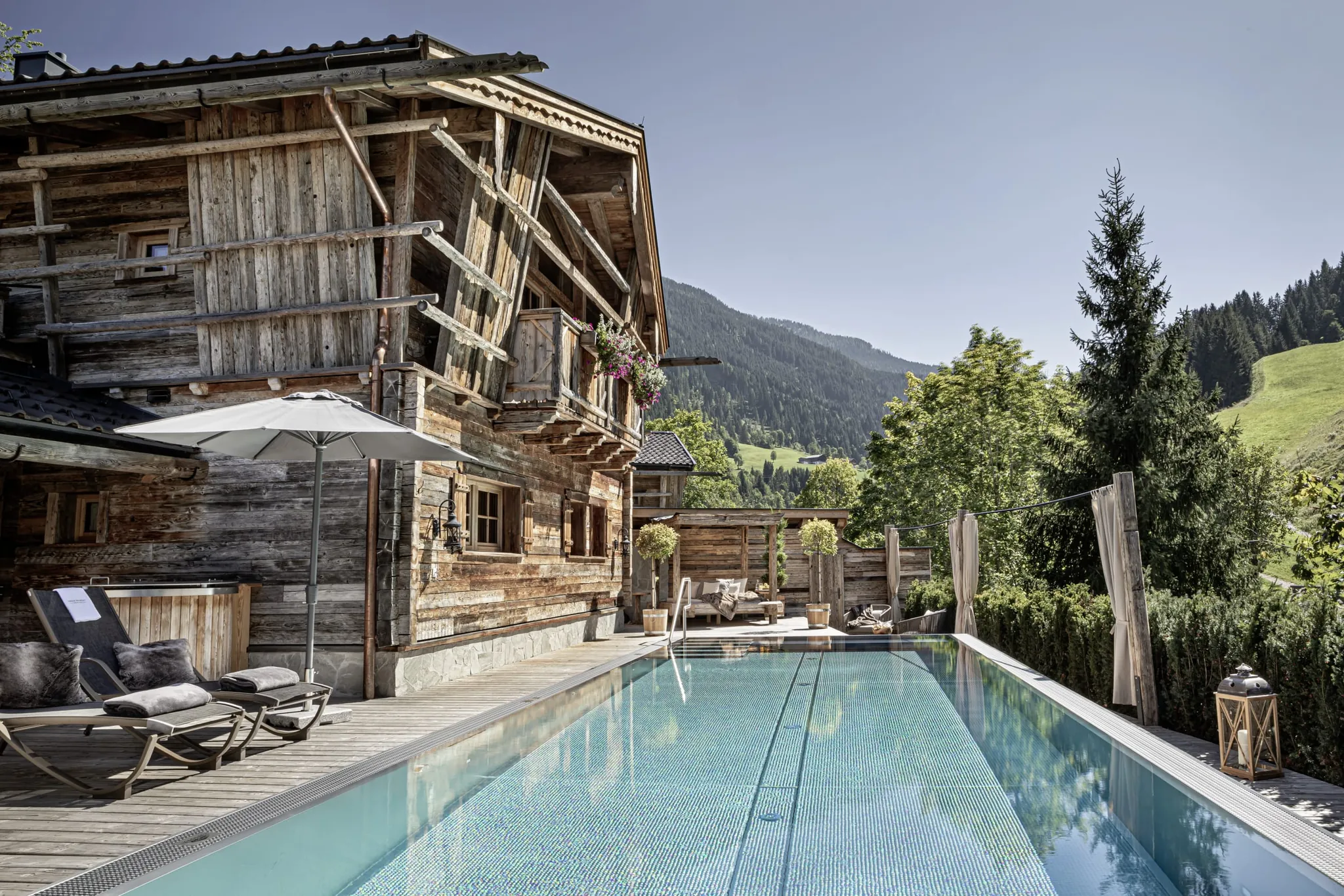 Blick auf den privaten Außenpool und die Pool Luxury Lodge des Bergdorfs Prechtlgut mit Sonnenliegen und Sonnenschirm