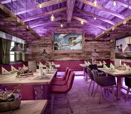 Restaurant des Bergdorfs Prechtlgut mit gedeckten Tischen, Hängelampen, pinkfarbenem Licht und pinkfarbenen Stühlen und Sitzbänken