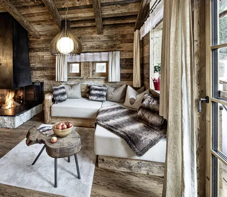Gemütliche Sitzecke mit Kissen, verglastem Kamin und Fernseher in einem der Chalets des Bergdorf Prechtlgut
