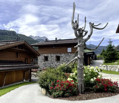 Außenanlage des Farm Resort Geislerhof mit Chalets und Berggipfeln im Hintergrund