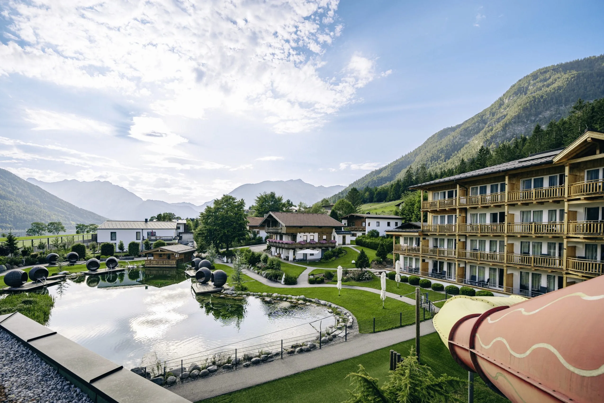 Außenanlage des Familienresort Buchau mit Naturbadeteich, Relaxkojen, Wasserrutsche und Bergpanorama