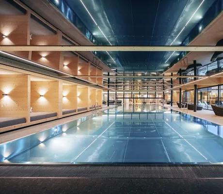 Beleuchteter Indoorpool mit Relaxkojen und bodentiefer Fensterfront mit Blick auf den Achensee des Familienresort Buchau
