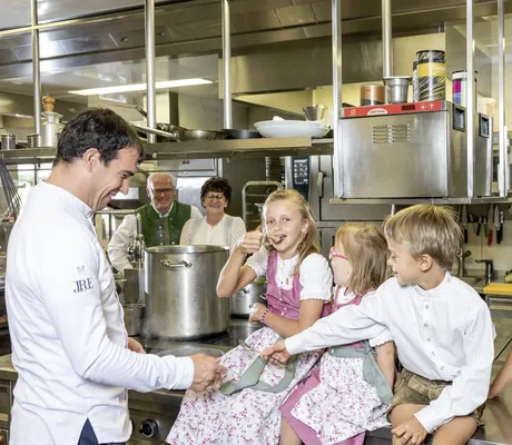 Kinder sitzen in der Küche der Riederalm auf dem Büffet und bekommen Probierlöffel vom Koch