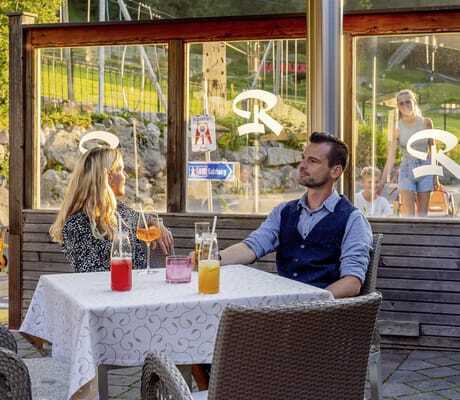 Paar sitzt mit Getränken am Tisch auf der Terrasse neben dem Spielbereich der Riederalm