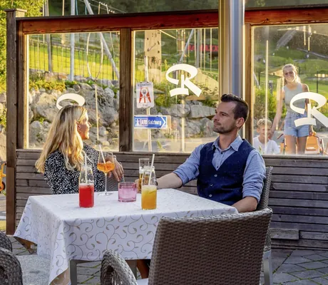Paar sitzt mit Getränken am Tisch auf der Terrasse neben dem Spielbereich der Riederalm