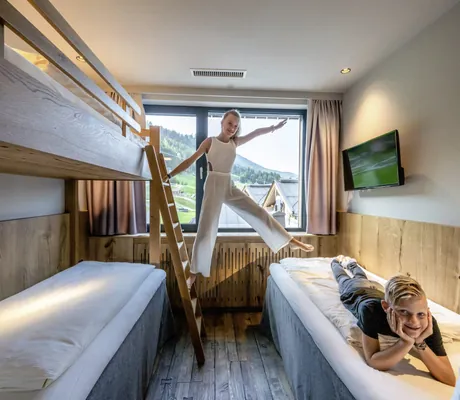 jugendliches Mädchen steht auf der Leiter des Hochbetts und Junge liegt auf dem Bett in der Riederalm