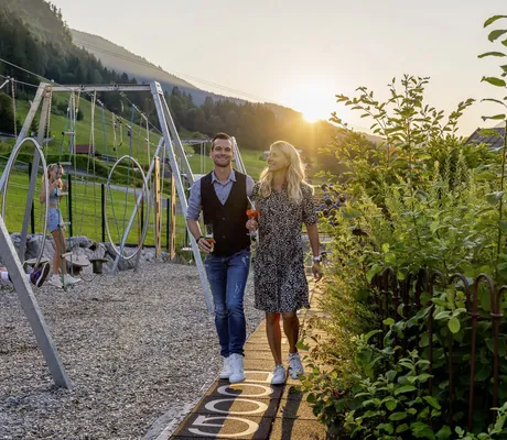 Paar mit Getränken läuft neben dem Kinderspielbereich auf dem Weg