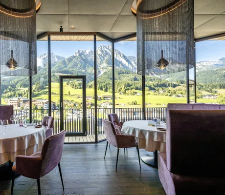 Restaurant mit rosa Sitzmöbeln und Perlenlampen in der Riederalm mit Blick auf die Leoganger Berge