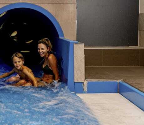 Frau in braunem BIkini und Junge kommen lachend aus der Wasserrutsche in der Riederalm