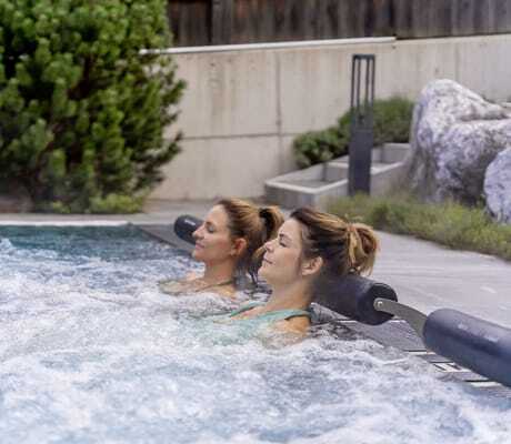 zwei Frauen liegen mit geschlossenen Augen in den Whirlliegen des Pools in der Riederalm