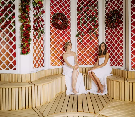 zwei junge Frauen mit Handtuch umgewickelt sitzen in einer mit Rosen dekorierten Sauna im Hotel Victory Therme Erding