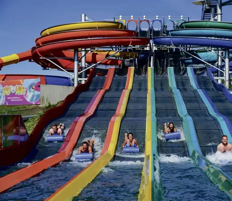 Sechs Personen rutschen die bunte Rainbow Wasserrutsche auf einer Matte herunter im Hotel Victory Therme Erding