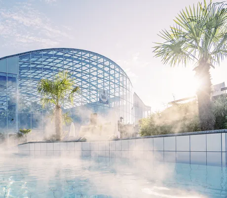 Blick auf das dampfende Outdoor-Wellenbad und die Außenansicht des Hotel Victory Therme Erding