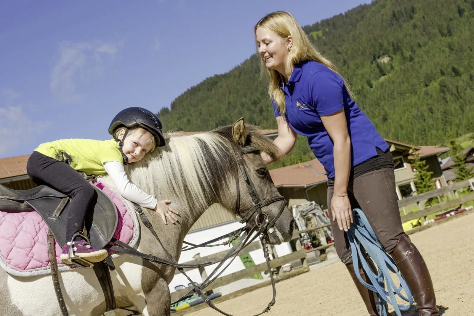 Kind schmiegt sich auf Pferder&uuml;cken w&auml;hrend Betreuerin die Z&uuml;gel h&auml;lt im Du-Familotel Krone