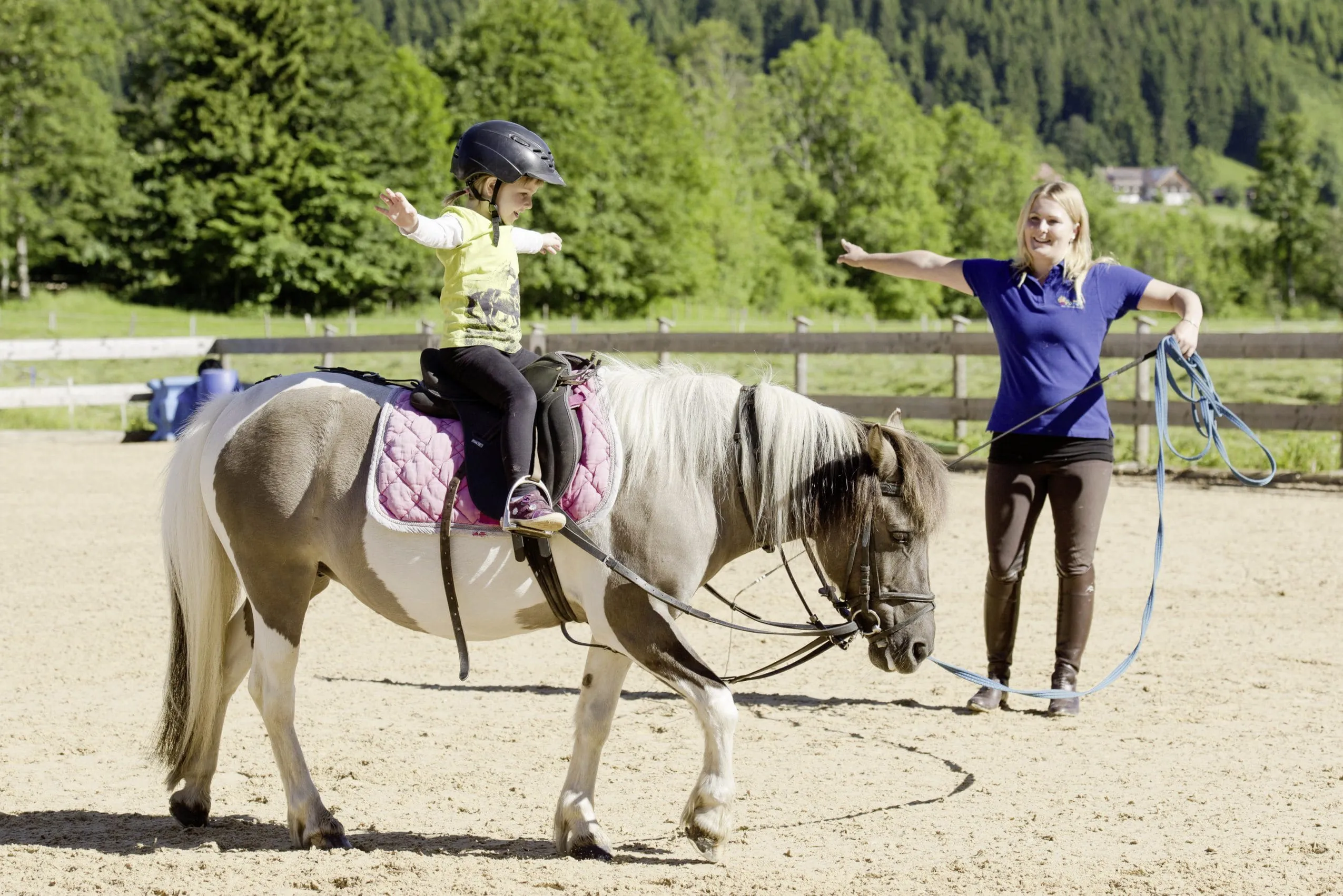Reitlehrerin und M&auml;dchen auf Pferd strecken die Arme aus bei Longier-&Uuml;bung des Du-Familotel Krone