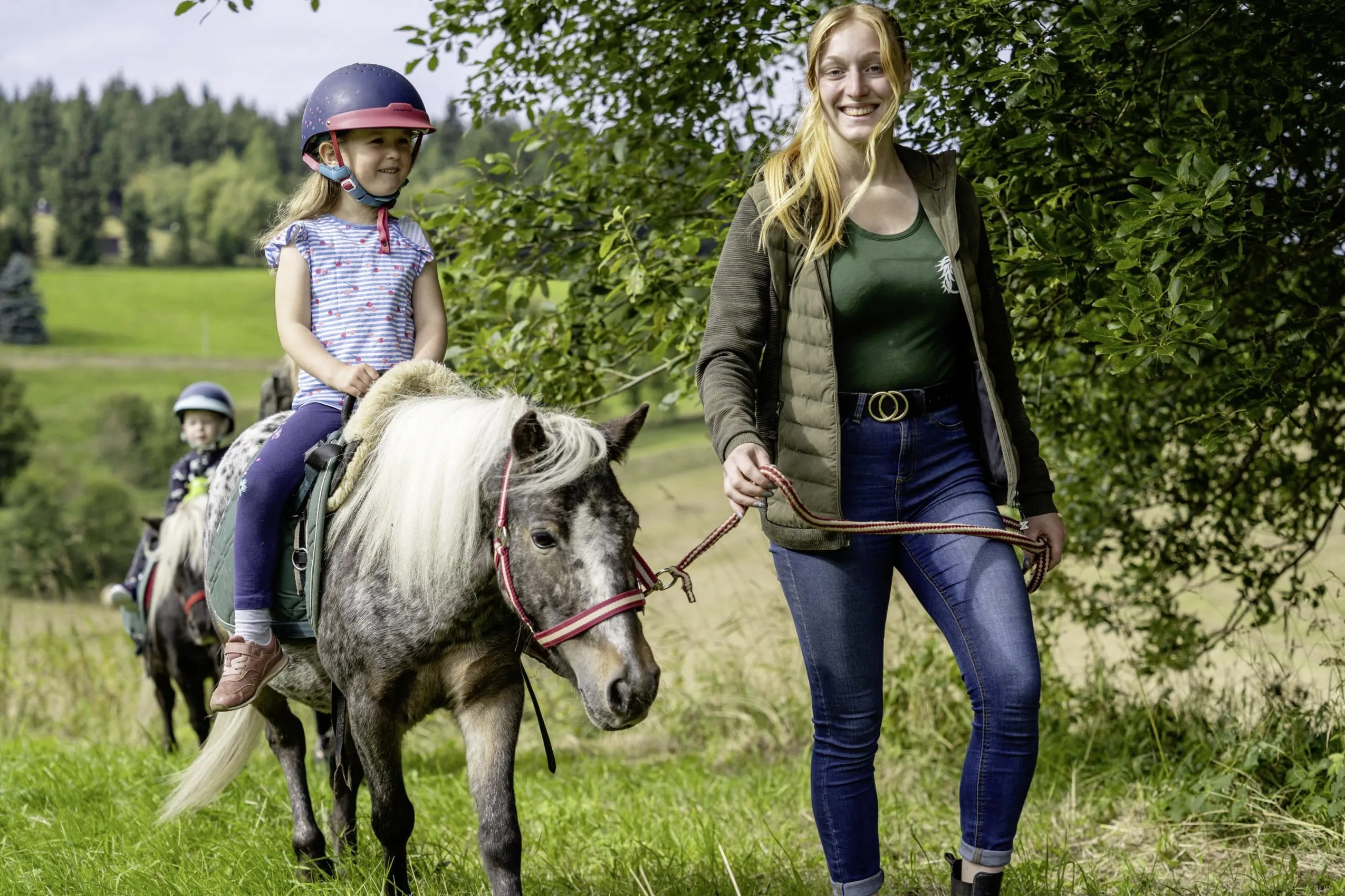 junges M&auml;dchen sitzt auf einem Pferd des Familotel Elldus Resort und Betreuerin h&auml;lt Strick
