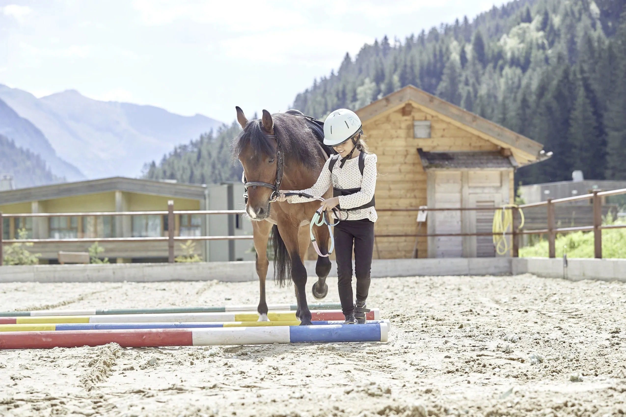 M&auml;dchen f&uuml;hrt braunes Pferd &uuml;ber Stangen im Feuerstein Nature Family Resort