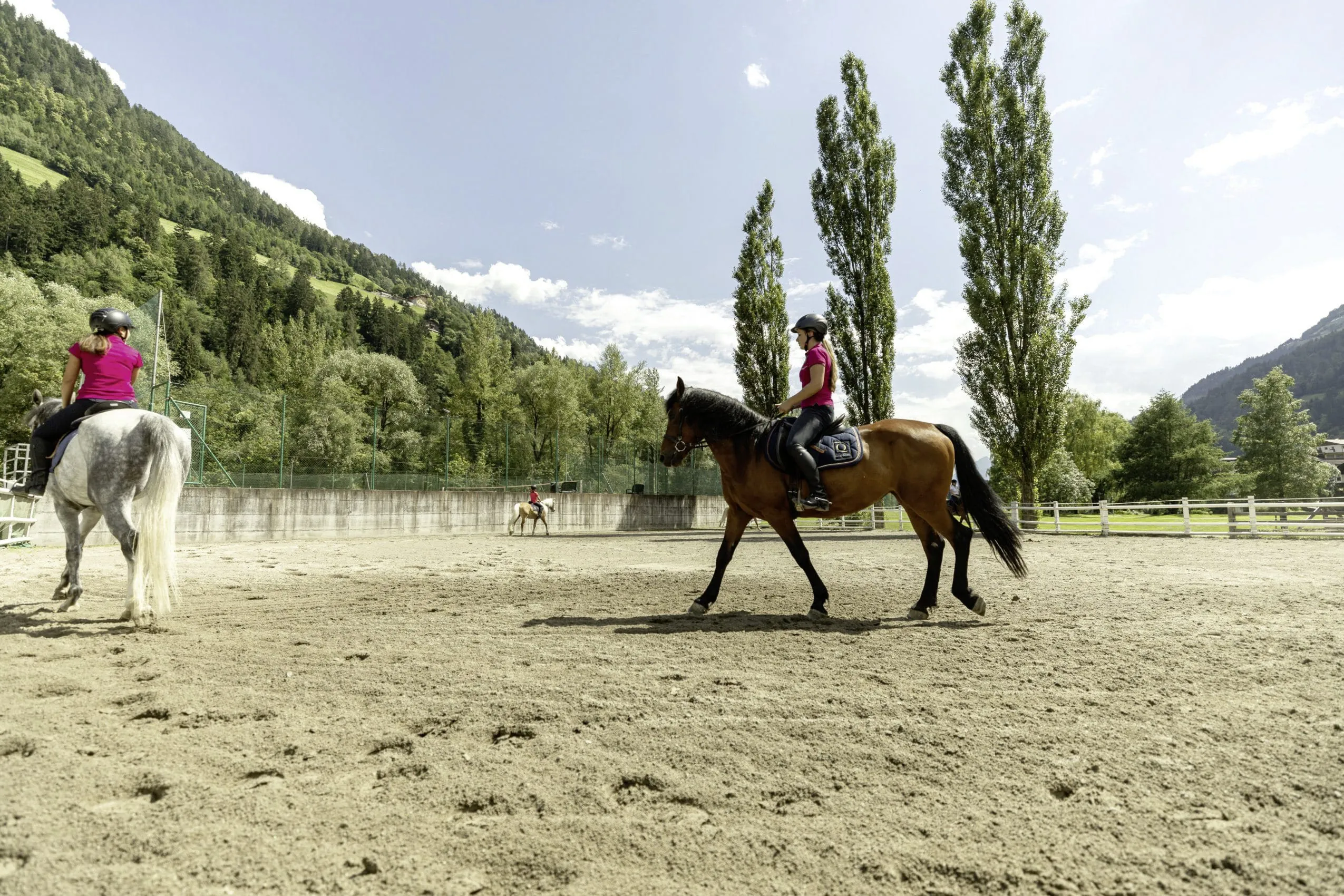 drei Reiter auf dem Au&szlig;enreitplatz des Quellenhof Luxury Resort Passeier